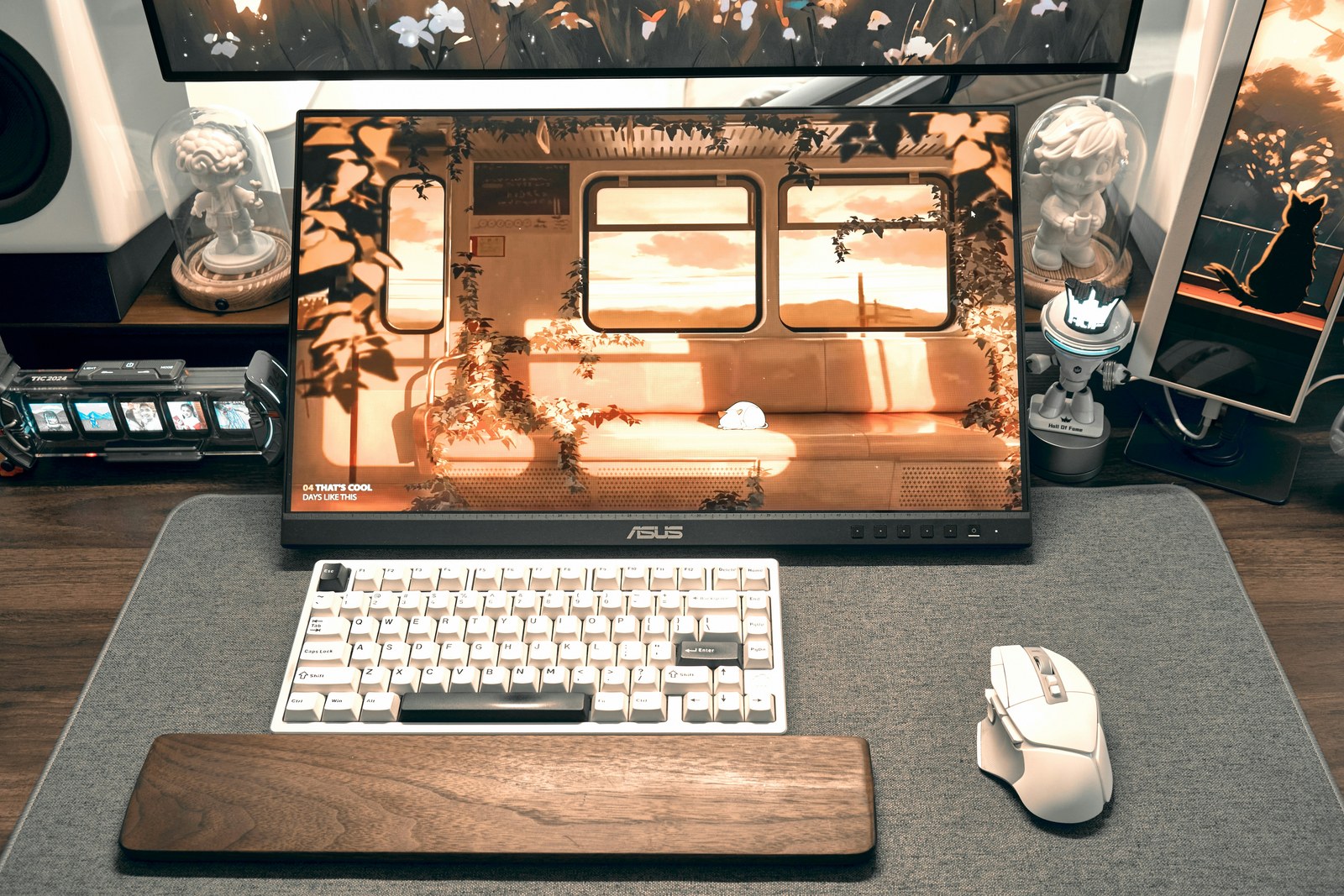 A desk with a large gray desk mat under a white keyboard and mouse, an ASUS monitor with a colorful wallpaper, and a wooden wrist rest.
