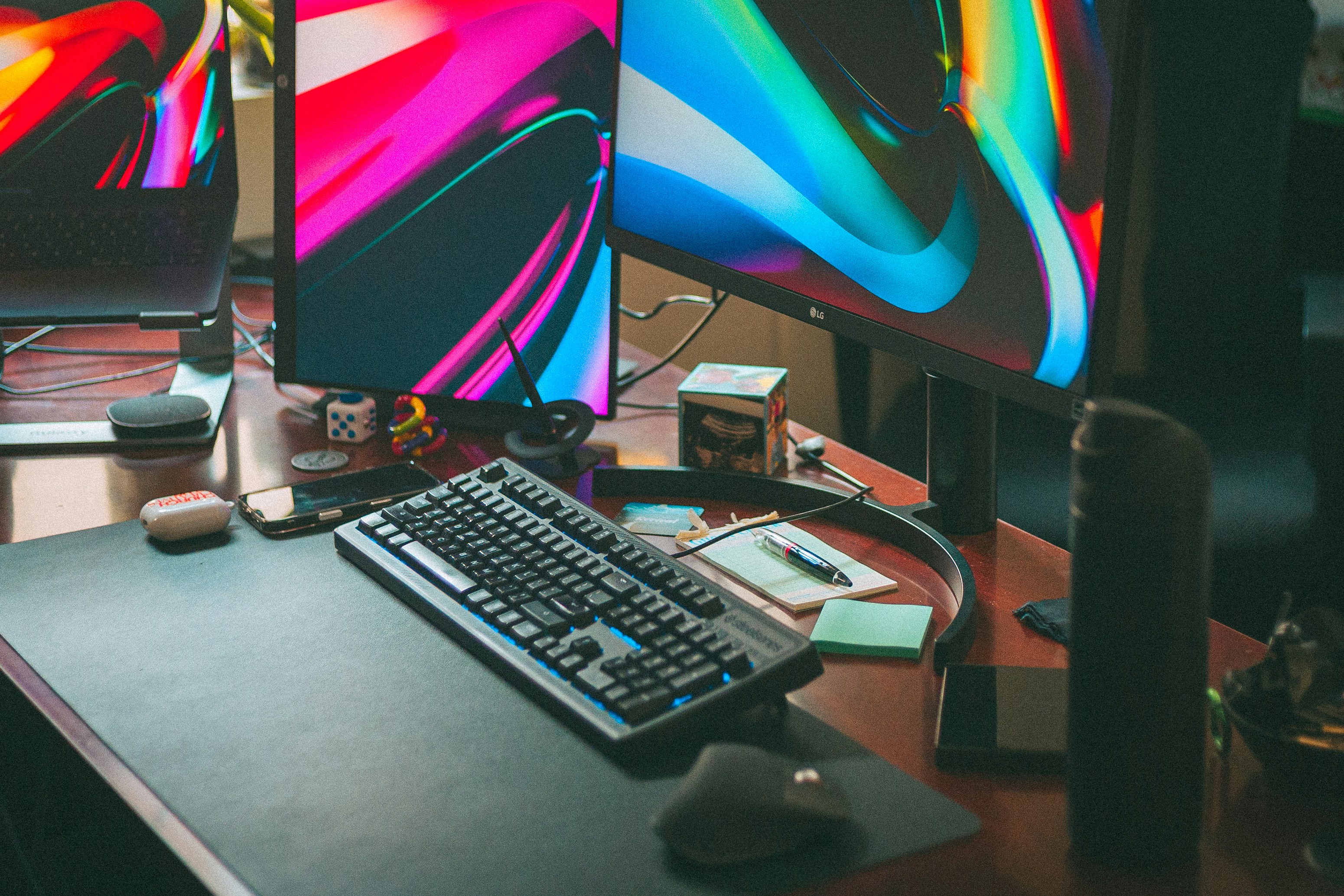 Two computer monitors displaying vibrant colorful screens side by side on a wooden desk.