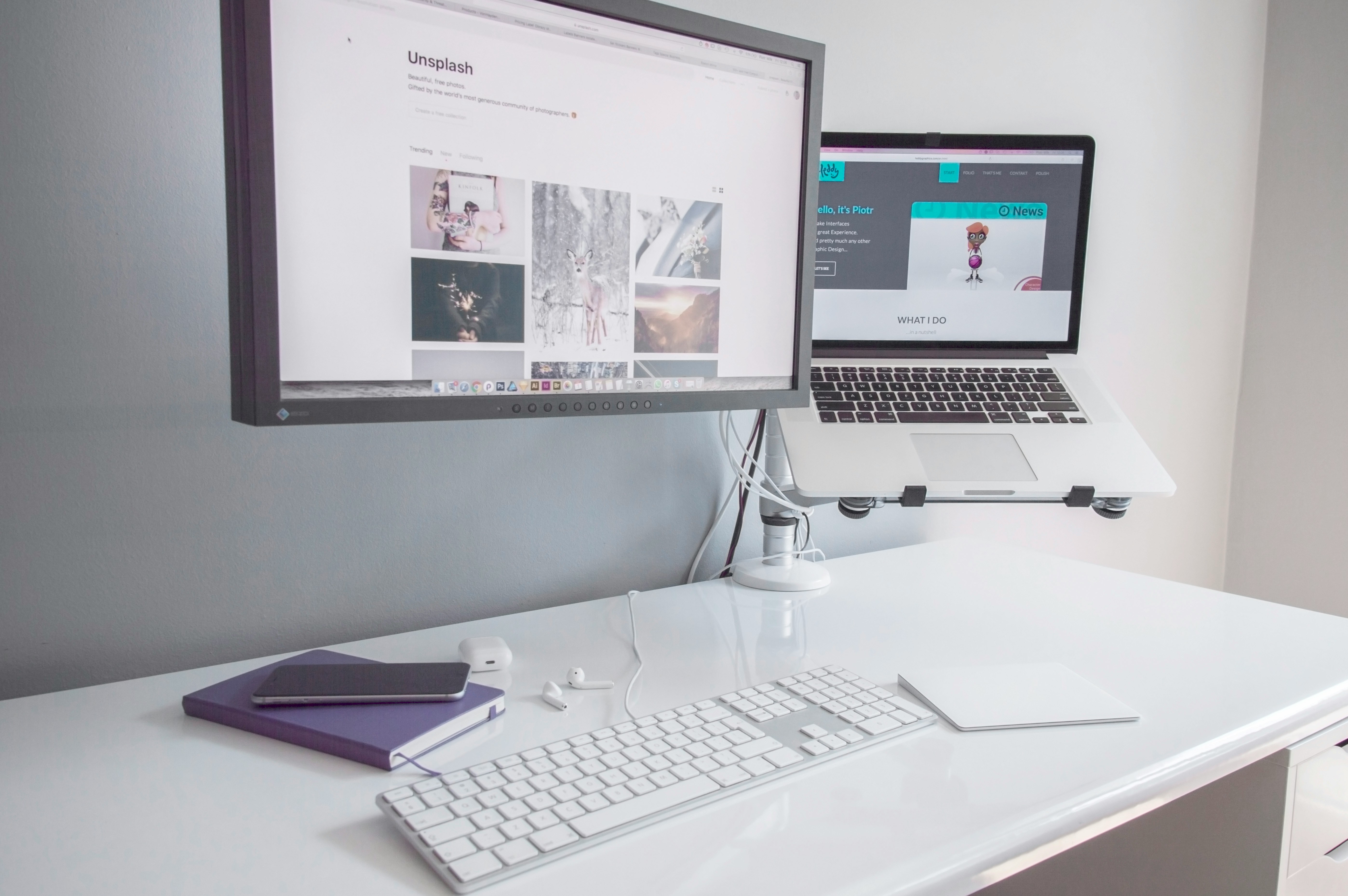 A white desk with a monitor mounted on an articulated arm beside a MacBook Air raised on a laptop stand.