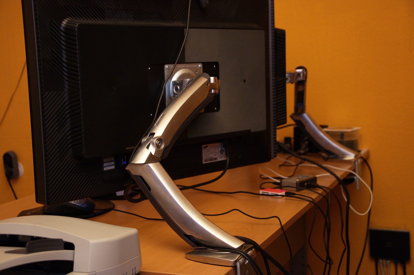 Silver single gas-spring monitor arm clamped to a wooden desk, holding one monitor (representative photo, not the ErGear model).